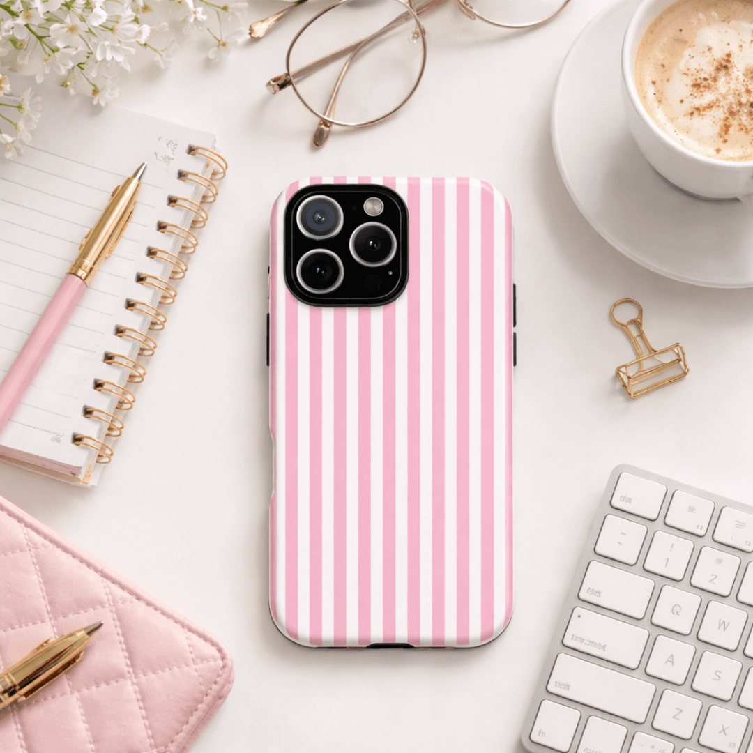 Tough phone case with pink and white stripes on a desk with a notebook, pen, glasses and coffee